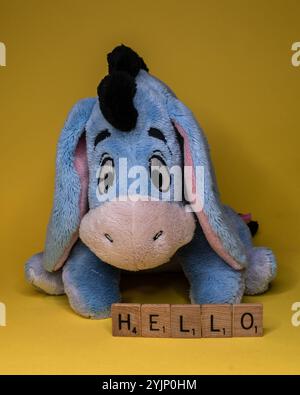 12 novembre 2024. Mascotte en peluche Eeyore winnie-the-Pooh assise sur un fond jaune avec des carreaux de lettres en bois scrabble avec le mot HELLO Banque D'Images