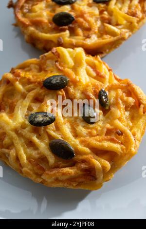 Galettes grillées de citrouille, rosti ou latkes, confectionnées à la fron de courge et de pomme de terre décorées de graines de citrouille en gros plan Banque D'Images