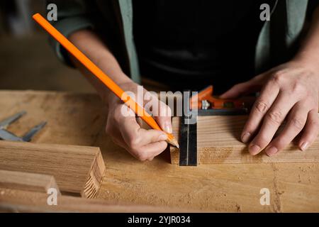 Un charpentier dédié se concentre intensément tout en marquant les mesures sur le bois dans un environnement d'atelier confortable. Banque D'Images