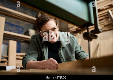 Une femme charpentière dévouée se concentre intentionnellement sur le façonnage du bois dans son atelier animé, entouré d'outils. Banque D'Images