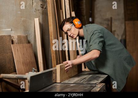 Un charpentier dévoué façonne habilement une pièce en bois, entourée d’outils et de matières premières dans son atelier. Banque D'Images