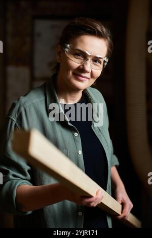 Une femme menuisière se concentre intensément sur son projet en bois, mettant en valeur son habileté et sa passion pour le travail du bois. Banque D'Images