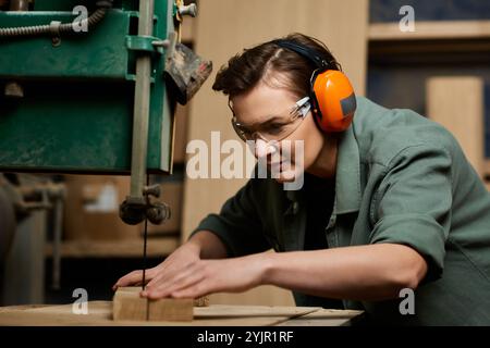 Une menuisière concentrée travaille habilement sur le bois dans son atelier, entourée d'outils et de matériaux. Banque D'Images