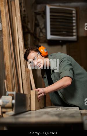 Une femme charpentier habile se concentre intensément alors qu'elle fabrique du bois dans son atelier, mettant en valeur son savoir-faire. Banque D'Images