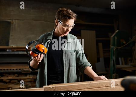 La menuisière se concentre intensément sur le façonnage du bois, entourée d’outils et de bois dans son atelier. Banque D'Images