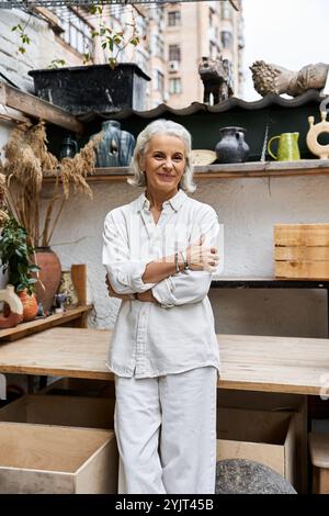 Une femme mature gracieuse pose dans son atelier artistique rempli de décorations et de plantes uniques. Banque D'Images