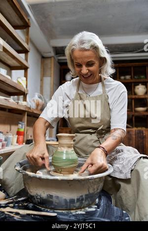 Une femme talentueuse fabrique joyeusement un beau pot sur la roue des potiers dans son espace de travail artistique. Banque D'Images