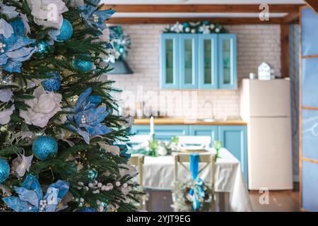 Sapin de Noël décoré de fleurs bleues et blanches en gros plan sur fond de cuisine turquoise. Salle de fête avec des décorations pour célébrer HO d'hiver Banque D'Images