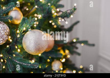 Arbre de Noël décoré avec des ornements festifs dorés et des lumières brillantes sur fond intérieur. Ambiance festive dans un espace intérieur confortable, parfait pour Banque D'Images