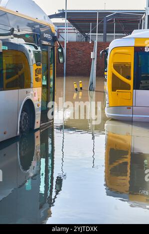 Viladecans. Espagne - 15 novembre 2024 : L'image montre une rue sous l'eau de la ville avec des bus visibles, illustrant les inondations causées par des pluies intenses. Banque D'Images