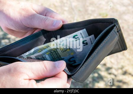 Homme dans la rue et tenant le leader noir partmone avec de l'argent en euros dans les mains. Billets dans le portefeuille pour le concept de commerce. Banque D'Images