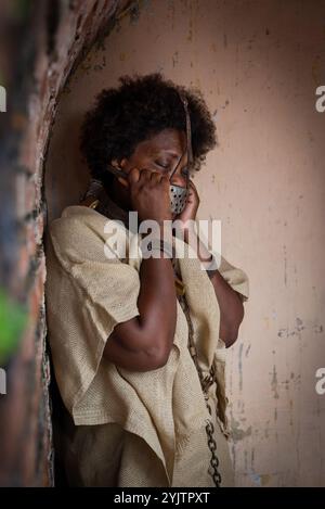 Femme noire enchaînée, touchant le masque de fer attaché à son visage avec un regard de peur. Représentation de l'esclave Anastacia. L'esclavage au Brésil. Banque D'Images