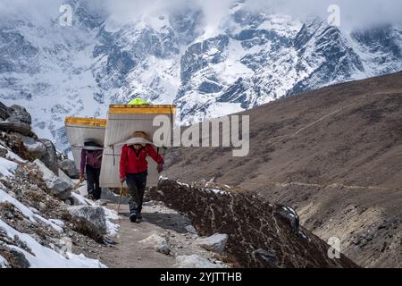 Deux jeunes porteurs sherpa portent des portes sur le dos dans la région de l’Everest, au Népal. Banque D'Images