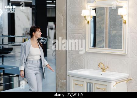 Une femme en costume gris clair se tient dans un showroom moderne, regardant vers le côté droit du cadre. Une grande baignoire blanche autoportante se trouve dans le Banque D'Images