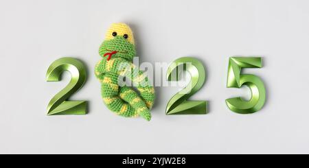 Jouet tricoté serpent vert rayé et numéros verts. Le symbole de l'année 2025 sur fond gris. Banque D'Images