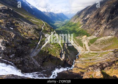 Une vue d'été à couper le souffle sur Trollstigen, Norvège, avec une cascade en cascade au premier plan et une vallée sinueuse qui s'étend au loin. Banque D'Images