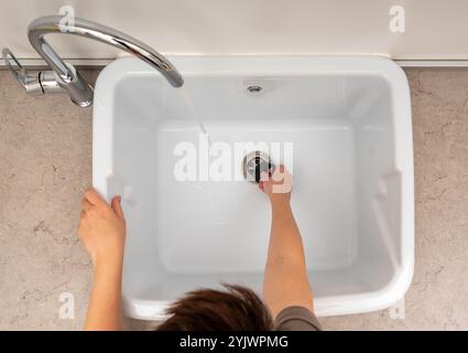 Vue rapprochée d'une personne nettoyant un évier utilitaire avec de l'eau courante d'un robinet. Banque D'Images