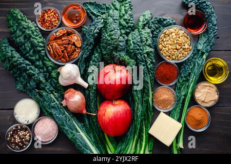 Ingrédients pour la salade de chou frisé avec noix confites, fromage et pommes : feuilles de chou frisé toscan, pommes croustillantes, noix, légumes et épices sur bois rustique Banque D'Images