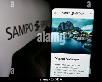 Dans cette illustration photo, une personne tient un téléphone portable avec la page Web de la compagnie d'assurance finlandaise Sampo Oyj devant le logo de l'entreprise. Banque D'Images