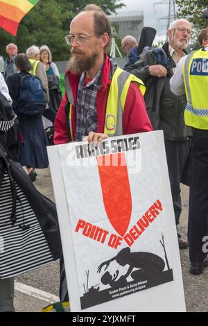 London, UK. 5th September 2017. A man holds a poster showing a bomb falling on a woman and child at he second day of protests against the world's largest arms fair held in London's docklands, 'No Faith in War' was a series of events organised by various faith groups. Before I arrived there had been a lock-in on the approach road stopping deliveries coming to set up the fair through the East gate. This was followed by a Quaker meeting at the side of the road during which a number of people stood or sat to block the road and several who refused to move were arrested. Then four protesters descend Stock Photo