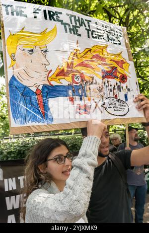 Londres, Royaume-Uni. 19 août 2017. Une femme tient une affiche graphique montrant Trump comme respirant le feu qui allume les torches des organisations nazies lors de la manifestation Stand Up to Trump soutenue par une vingtaine d'organisations, dont le CWU, NUT, Unite, UCU, CND, stop the War, Campaign Against Climate change, Muslim Association of Britain et d'autres manifestent devant l'ambassade américaine. Ils disent que la rhétorique sectaire de Trump sème la haine et la division, encourageant les groupes d'extrême droite responsables d'événements tels que ceux de Charlottesville et condamnant son bellicisme en menaçant une guerre nucléaire Banque D'Images