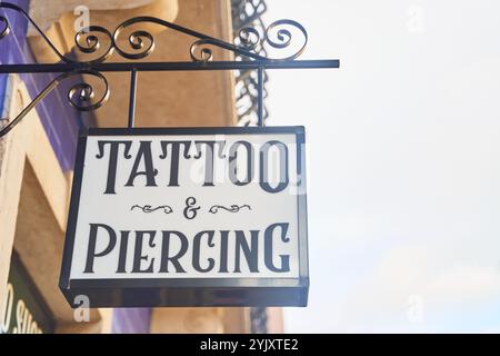 Un panneau avec une police en gras est accroché à un poteau sur le côté du bâtiment montrant le magasin de tatouage et de piercing, ajoutant un luminaire avant-gardiste à la façade Banque D'Images