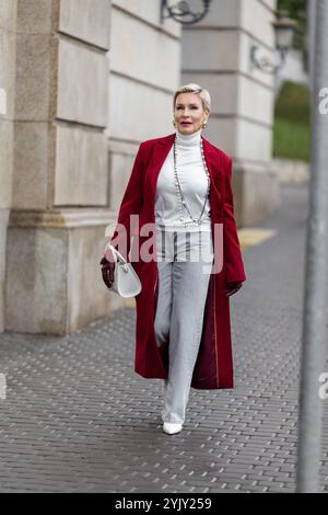 Femme élégante en Bourgogne Coat Walks City Street. Porter des vêtements à la mode chandail blanc à col roulé, collier de perles et Jeans gris, portant blanc Banque D'Images