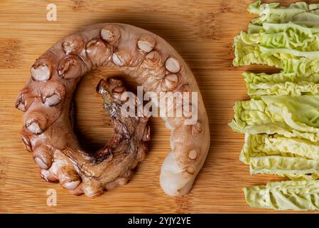 Cuisse de poulpe séchée non cuite avec des morceaux de chou sur une planche de bois. Banque D'Images
