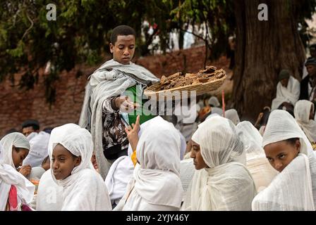 Altar Boy distribue du pain béni aux croyants en vêtements traditionnels blancs Shamma après le service du dimanche, Lalibela, Ethiopie Banque D'Images