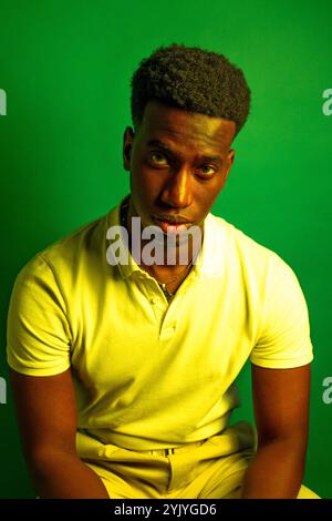Portrait d'un jeune homme sérieux portant un polo blanc et un pantalon beige, posant sur un fond vert éclatant Banque D'Images