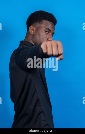 Jeune homme portant une chemise noire jetant un coup de poing sur un fond bleu vif Banque D'Images