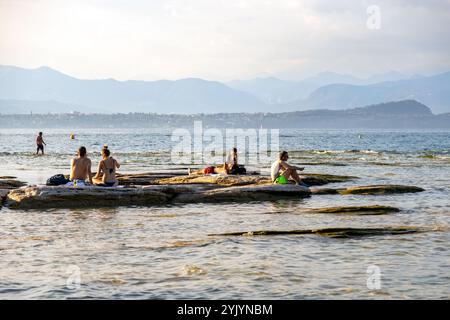 Sirmione, Italie - Sep 21st, 2024 : les gens se détendent sur les rochers du lac, en profitant de la vue sereine sur le lac de Garde Banque D'Images