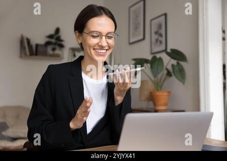 Femme d'affaires souriante tenant smartphone dirigeant la conversation à l'aide du haut-parleur Banque D'Images