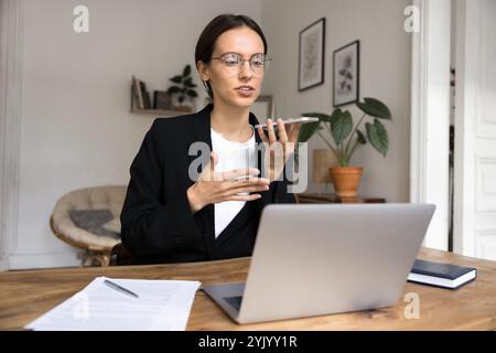 Femme d'affaires utilisant la fonction de haut-parleur sur la conversation principale de cellule dans le bureau Banque D'Images