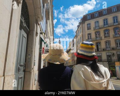 Lisbonne, Portugal - femmes touristes en chapeaux colorés marchant dans une rue du centre-ville avec de vieux bâtiments par une journée ensoleillée, vue arrière. Voyage en famille dans la ville Banque D'Images