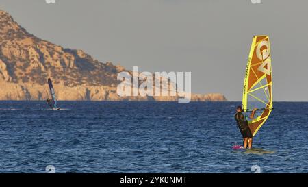 Planche à voile naviguant devant une toile de fond rocheuse dans la mer bleue, planche à voile, spot de planche à voile Meltemi, Devils Bay, Paralia Vatha, plage de Vatha, sud-e. Banque D'Images