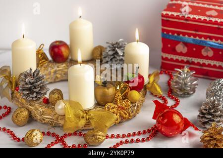 Couronne de l'Avent avec quatre bougies allumées, collier de perles rouges et décorations de Noël à côté Banque D'Images