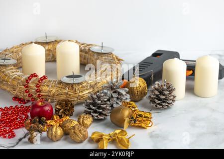 Scène artisanale avec couronne de l'Avent, bougies blanches, matériel de décoration et un pistolet à colle sur une surface en marbre Banque D'Images