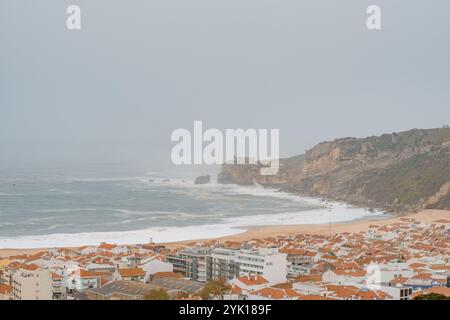 Vue surélevée sur les falaises de bord de mer, plage de sable et une ville résidentielle avec des toits de tuiles rouges sur une journée brumeuse Banque D'Images