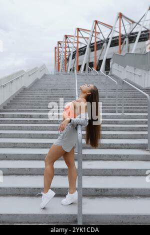Une femme en short se tient sur un escalier en bois devant un stade Banque D'Images