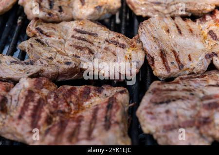Vue détaillée des steaks de porc cuisant sur un gril, avec des lignes carbonisées et de l'essence fumée, parfait pour le barbecue et les thèmes liés à la nourriture. Banque D'Images