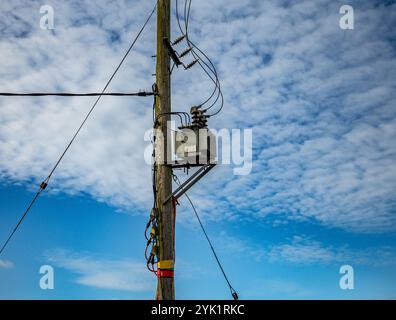 Poteau électrique avec transformateurs et fils contre un ciel bleu éclatant avec des nuages blancs dispersés Banque D'Images