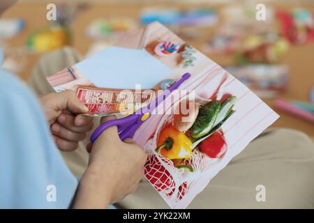 Création d'un tableau de vision. Petit garçon découpant la photo à l'intérieur, gros plan Banque D'Images