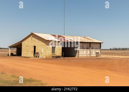 Scène de paysage d'une route de gravier à l'entrée d'un ancien hangar de ferme avec un toit en tôle ondulée dans l'Outback, Australie. Banque D'Images