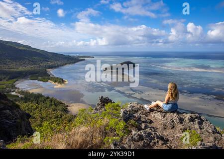 Jeune femme assise sur un rocher et profitant de la vue sur le lagon et la côte à mi-chemin de la randonnée vers la montagne le Morne, le Morne, rivière Banque D'Images