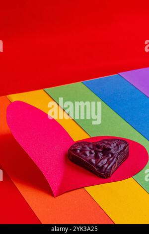 concept lgbt, coeur en chocolat sur papier rouge sur drapeau arc-en-ciel sur fond rouge Banque D'Images