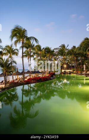 Piscine et parasols en chaume avec cocotiers au Royal Palms Beachcomber Luxury (Beachcomber Resorts) au crépuscule, Grand Baie, rivière du Rempar Banque D'Images