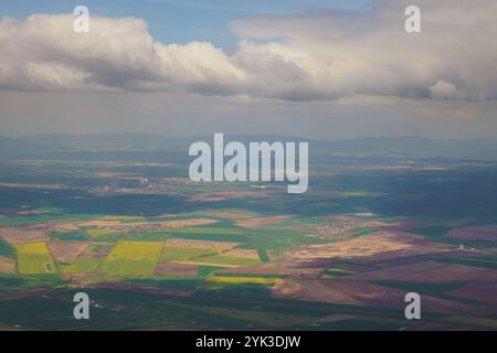 Cela capture une vue aérienne époustouflante de vastes terres agricoles avec des taches vertes, jaunes et brunes vibrantes sous un ciel bleu avec des nuages. Le paysage met en valeur l'agriculture rurale. Banque D'Images