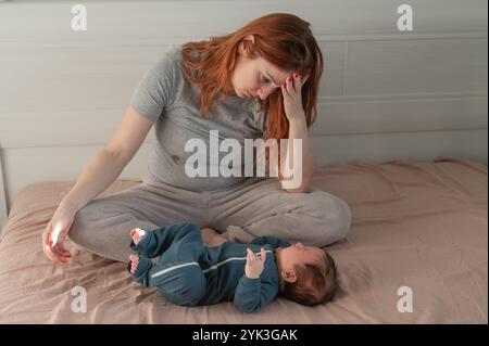 Une femme caucasienne est assise sur un lit à côté d'un bébé qui pleure. Dépression du post-partum. Banque D'Images