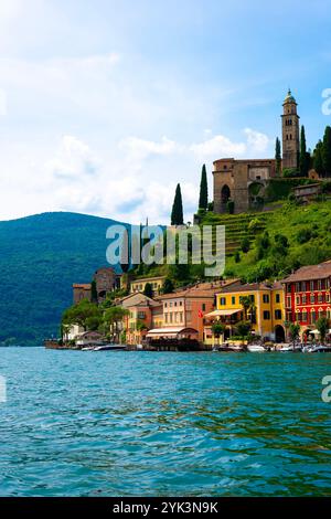 Maison et église sur la chaîne de montagnes dans une journée d'été ensoleillée sur le front de mer au lac de Lugano à Morcote, Lugano, Tessin, Suisse. Banque D'Images